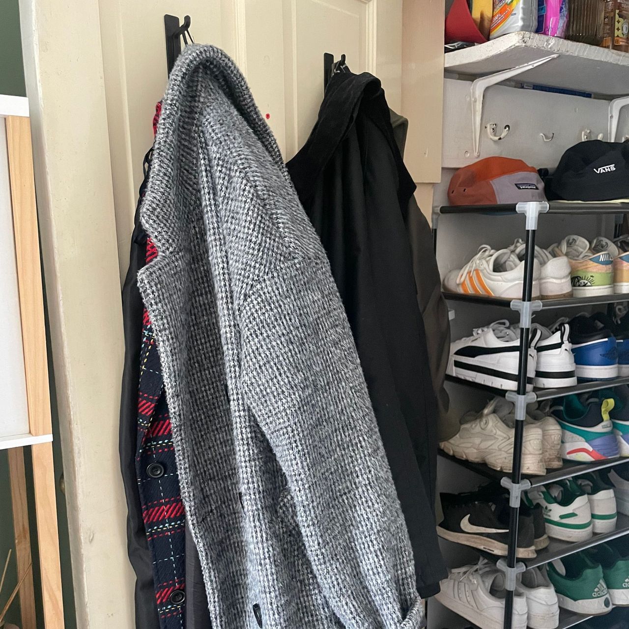 Coats hanging on the inside of a door in under-the-stairs cupboard next to a shoe rack