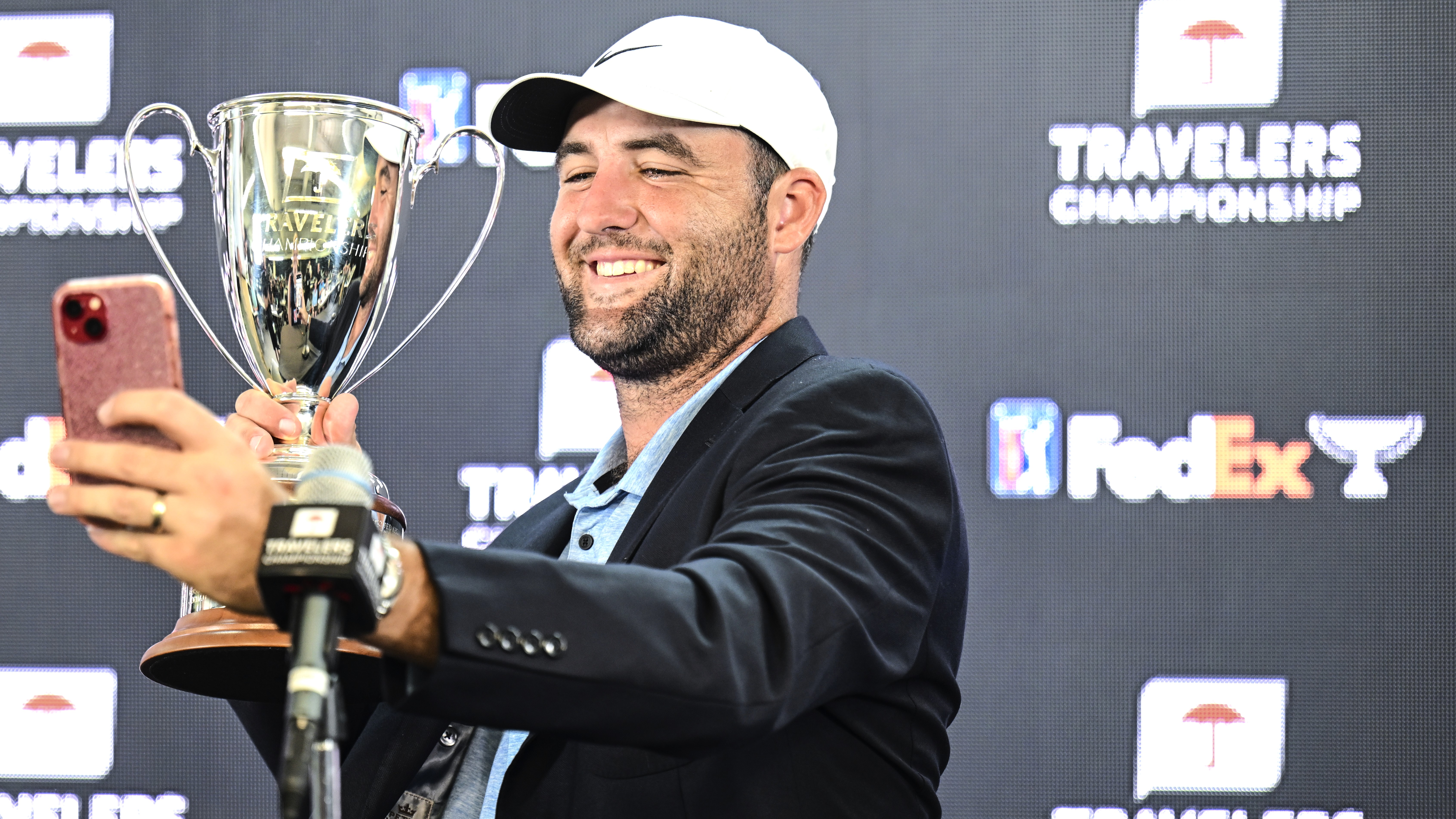 Scottie Scheffler takes a selfie with him holding the Travelers Championship trophy at the press conference