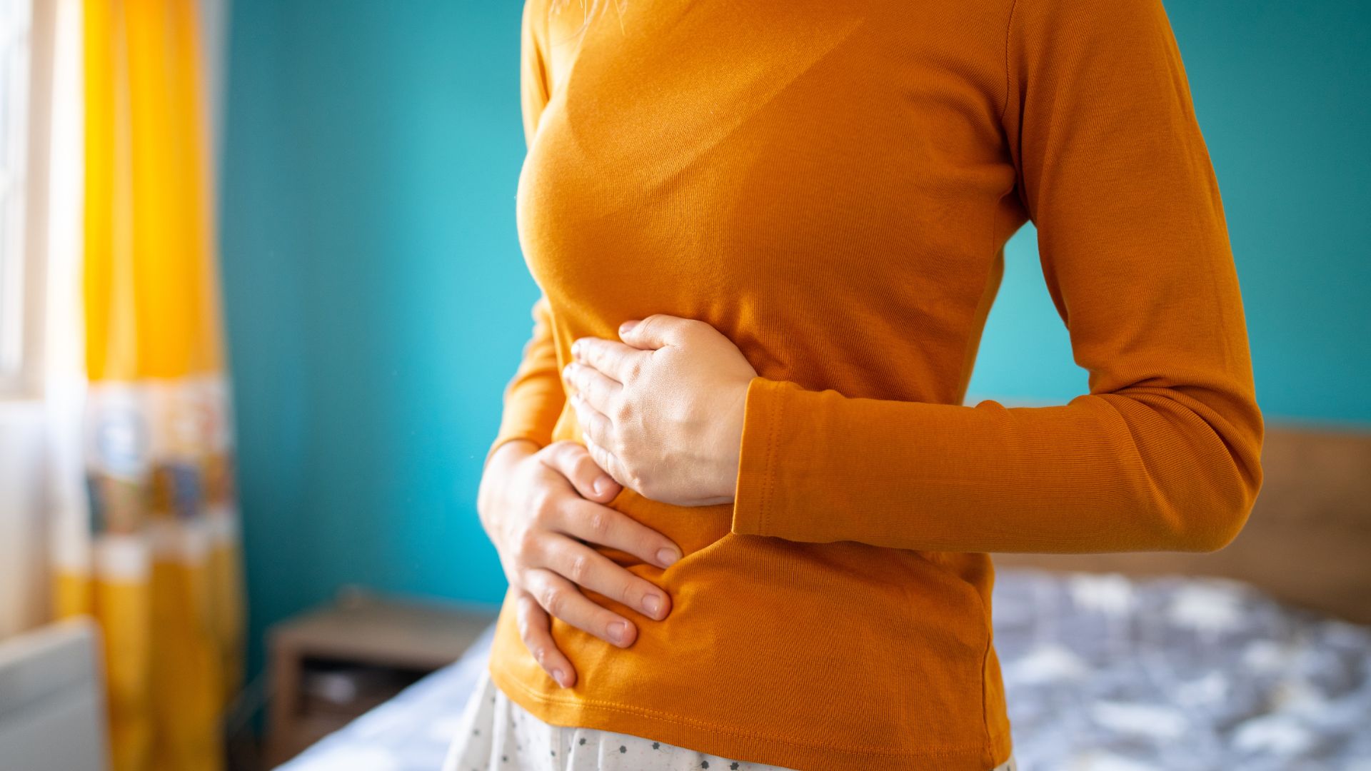 A woman wearing an orange long-sleeved t-shirt holds her stomach with both hands.