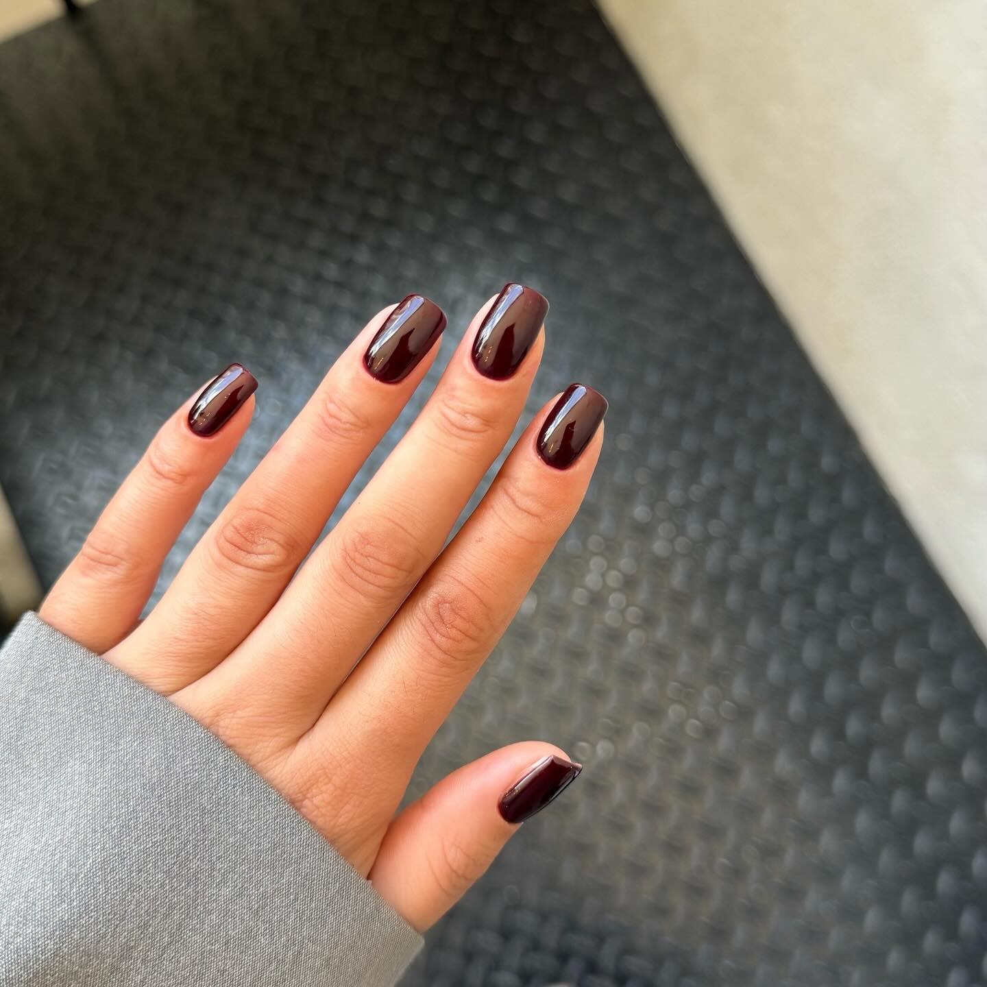 A picture of a woman's hand with a long, square-shaped dark burgundy manicure