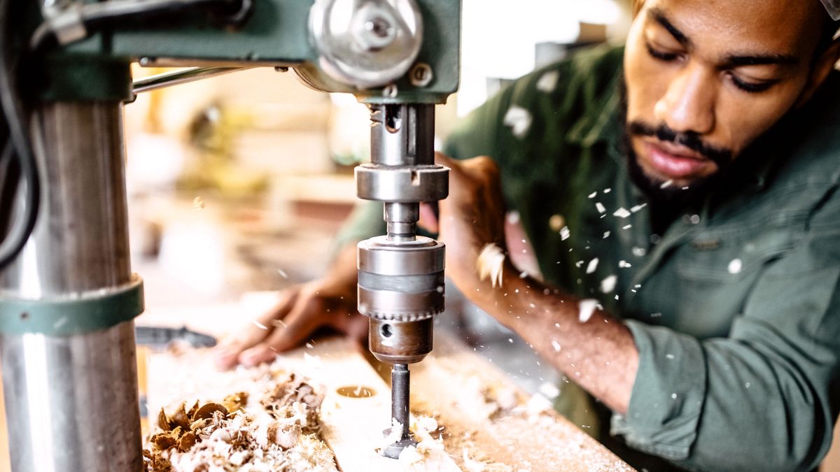 Close up of man using a pillar drill to drill into wood