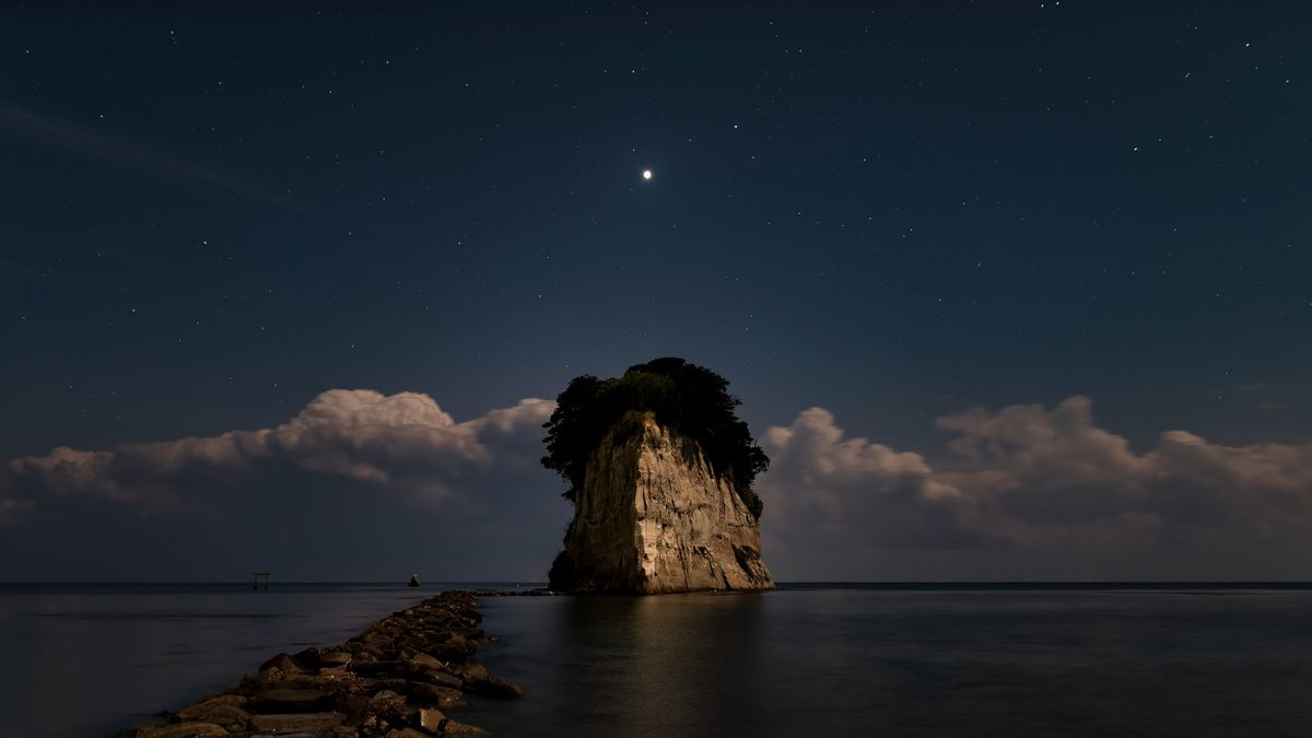 venus in the night sky above a rock in the ocean