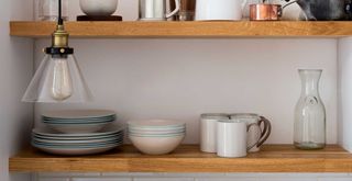 Close up of a kitchen shelf with plates, cups and other crockery with a glass pendant hanging above to show a few of the things you declutter before 2024