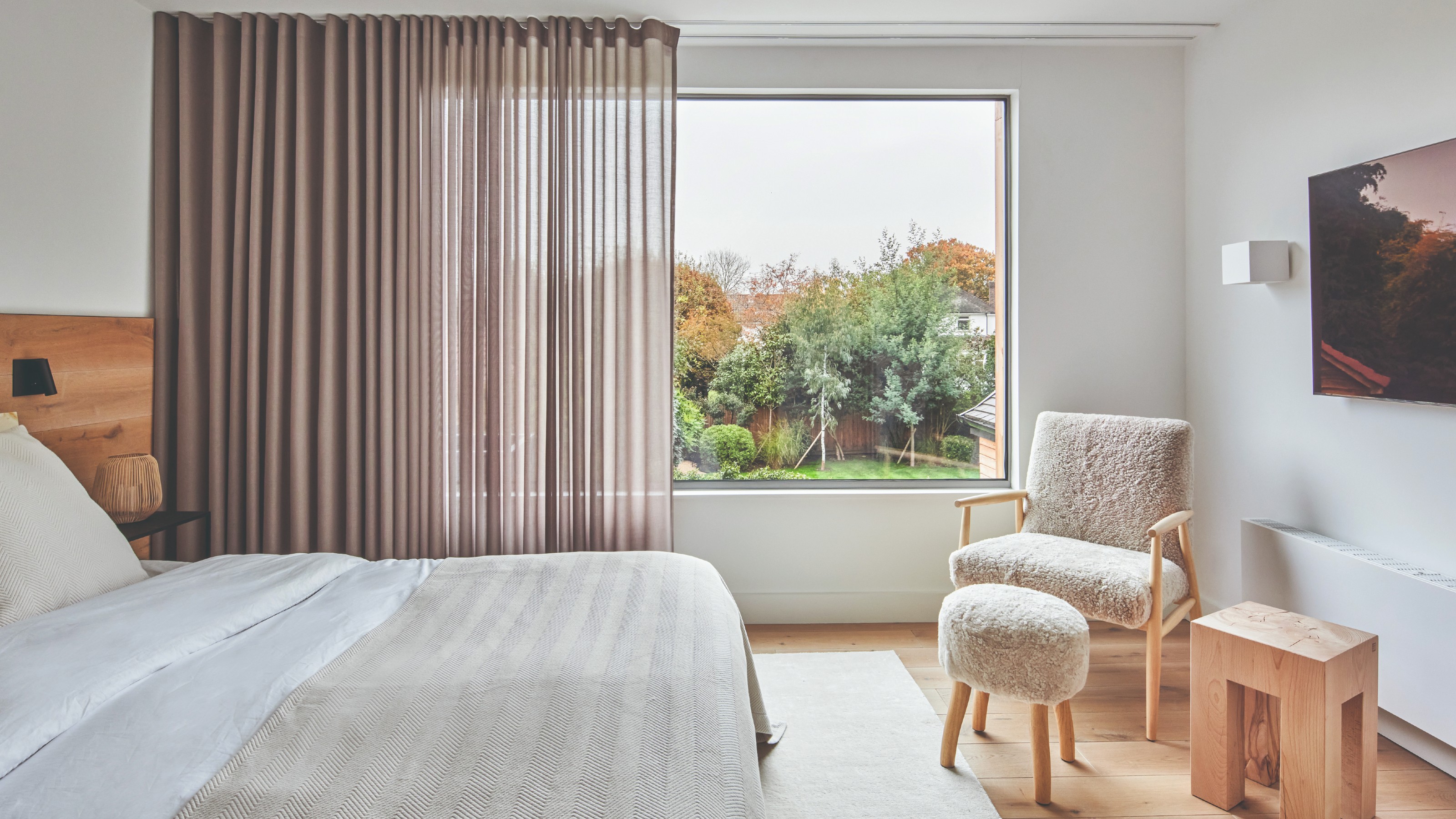 A minimalist bedroom with semi-sheer brown curtains and a shaggy accent chair with a matching stool
