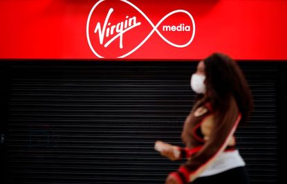 Person wearing a face mask walking past a Virgin Media sign