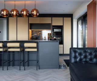 kitchen with black and pale wood units, island with barstools and amber glass ceiling pendants