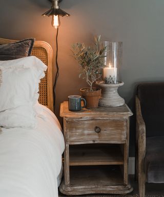winter decor ideas, cozy bedroom with limed nightstand, plant, candle, rattan and wood bed, white bedding, brass wall light