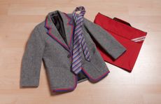 A flat lay image of a grey and red school blazer, tie and bag.