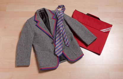 A flat lay image of a grey and red school blazer, tie and bag.