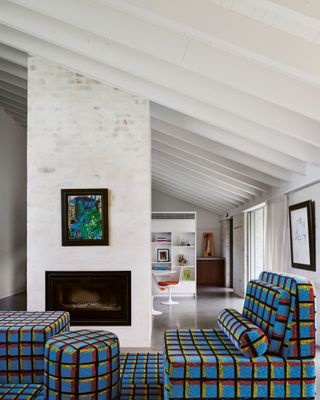 modern living rom with fireplace, angled roof, limewash brick walls, and patterned check sofa with matching ottoman and rug