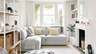 Small white living room with white l-shaped sofa and storage with shelves to demonstrate how to make a small living room look bigger