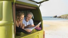 A retired couple smile as they look at a map in the back of their camper van.