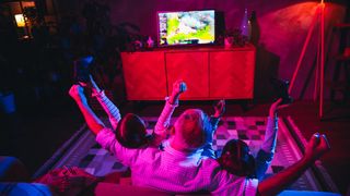 A father and his two children gaming in a cozy living room with coloured lighting