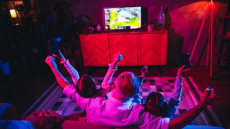 A father and his two children gaming in a cozy living room with coloured lighting