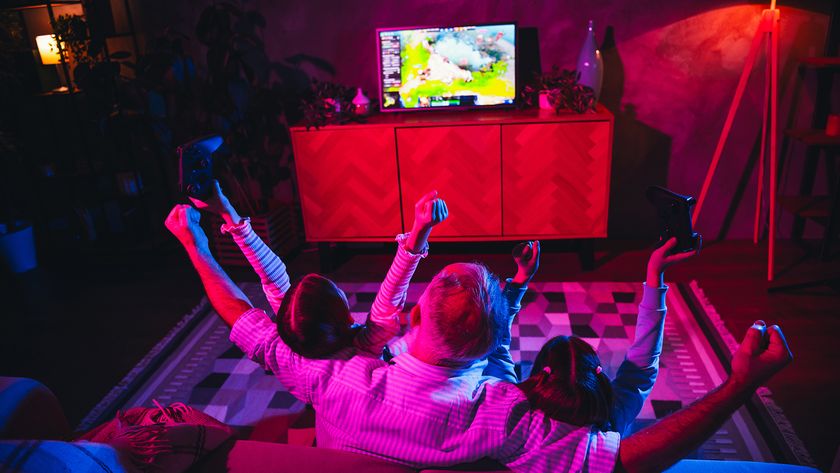 A father and his two children gaming in a cozy living room with coloured lighting