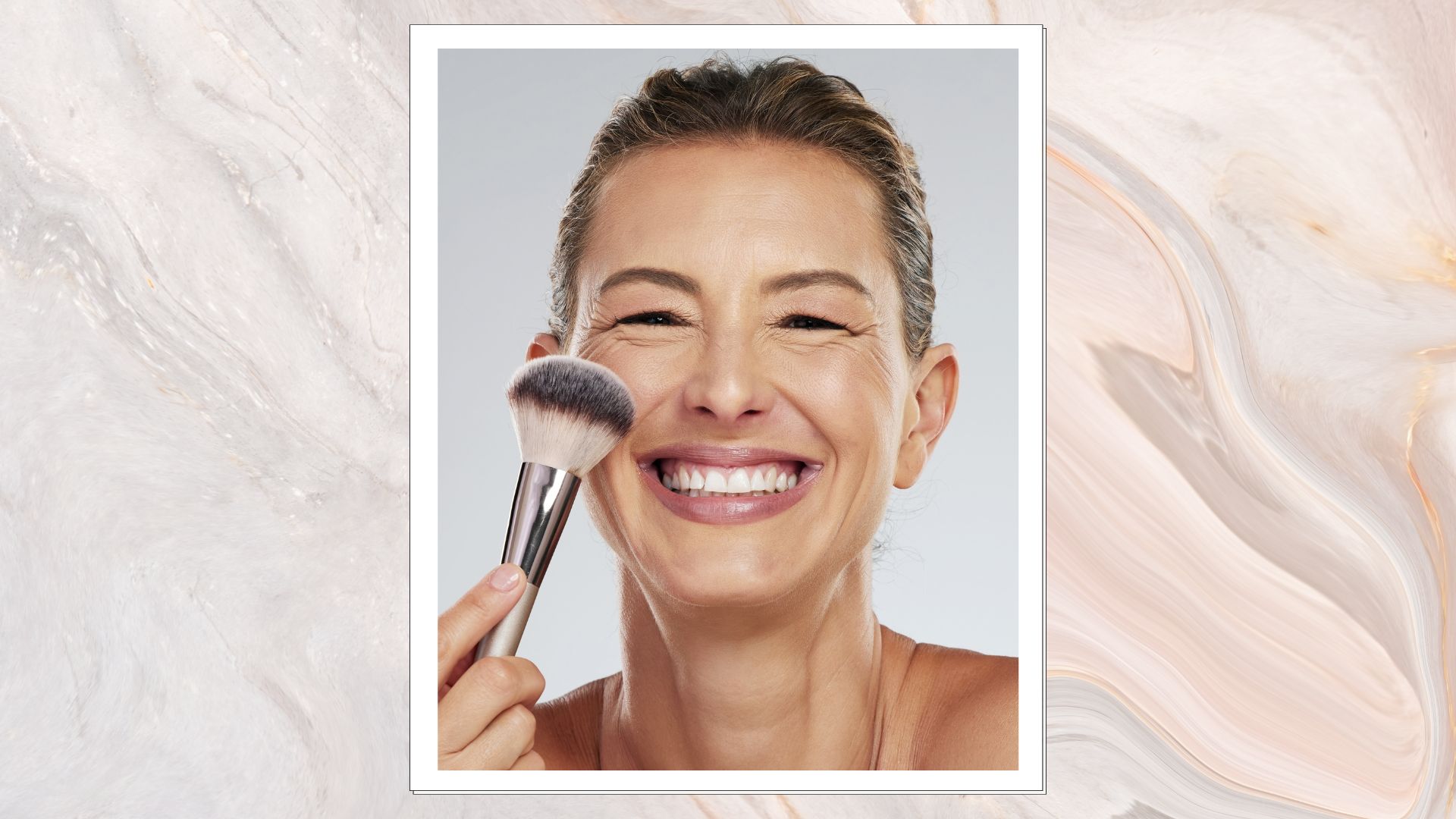 A marble-effect frame containing an image of a woman's face, smiling with glowing skin and her hair tied back, holding a blusher brush up to her cheek