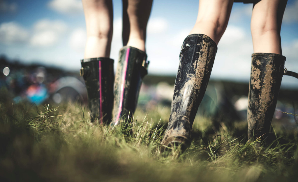 A close up of two people wearing muddy wellies at a festival