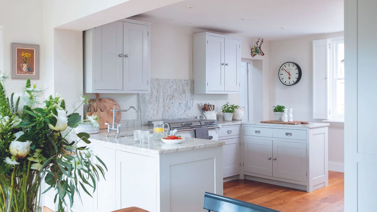 small grey kitchen with a mix of wall and floor cabinetry and marble splashback and wooden flooring with close up of flowers in corner