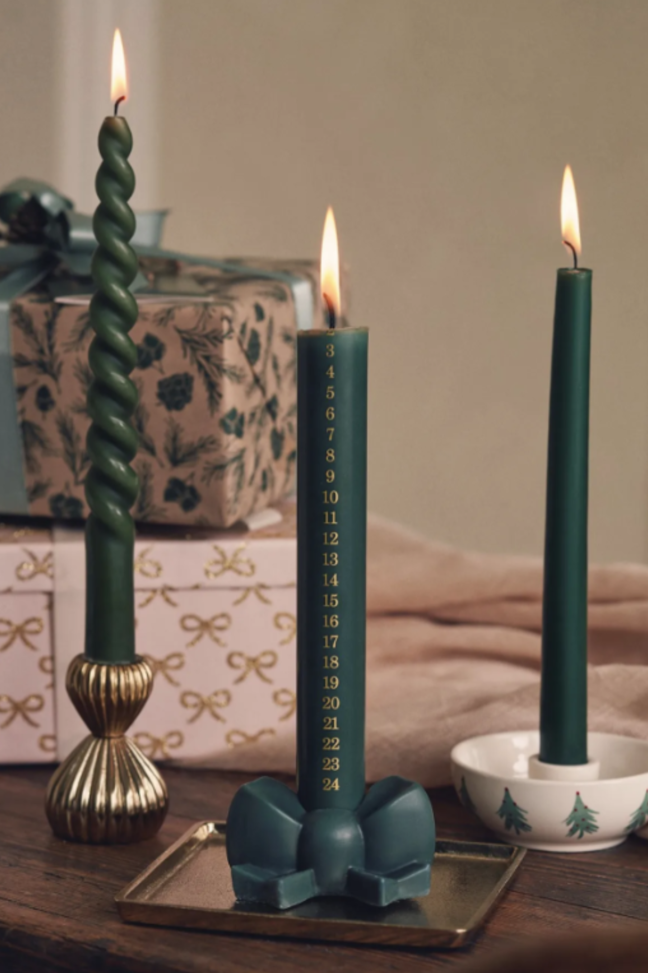 A advent taper candle in pine green in a bow holder beside other tapers