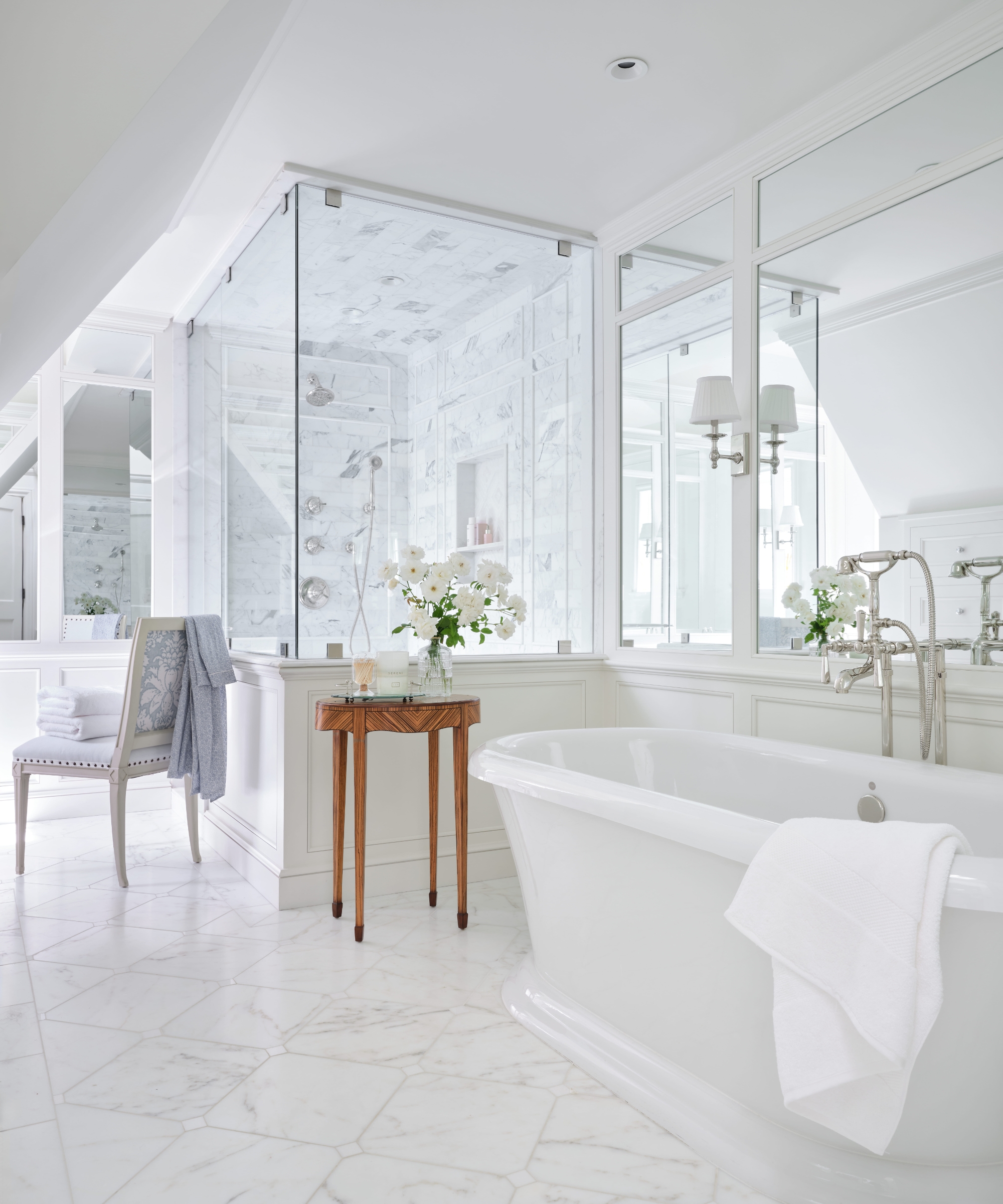 White primary bathroom with a freestanding tub, marble floor, glass shower, paneled cabinetry and mirrored walls.