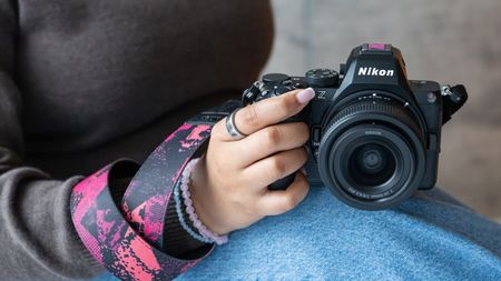 A person holds a Nikon camera with a colorful limited edition strap and hot shoe cover