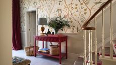 hallway with floral wallpaper above chair rail, stone painted underneath, red console and drapes, stone floor tiles, lamp, baskets, runner on stairs, Georgie Wykeham Designs