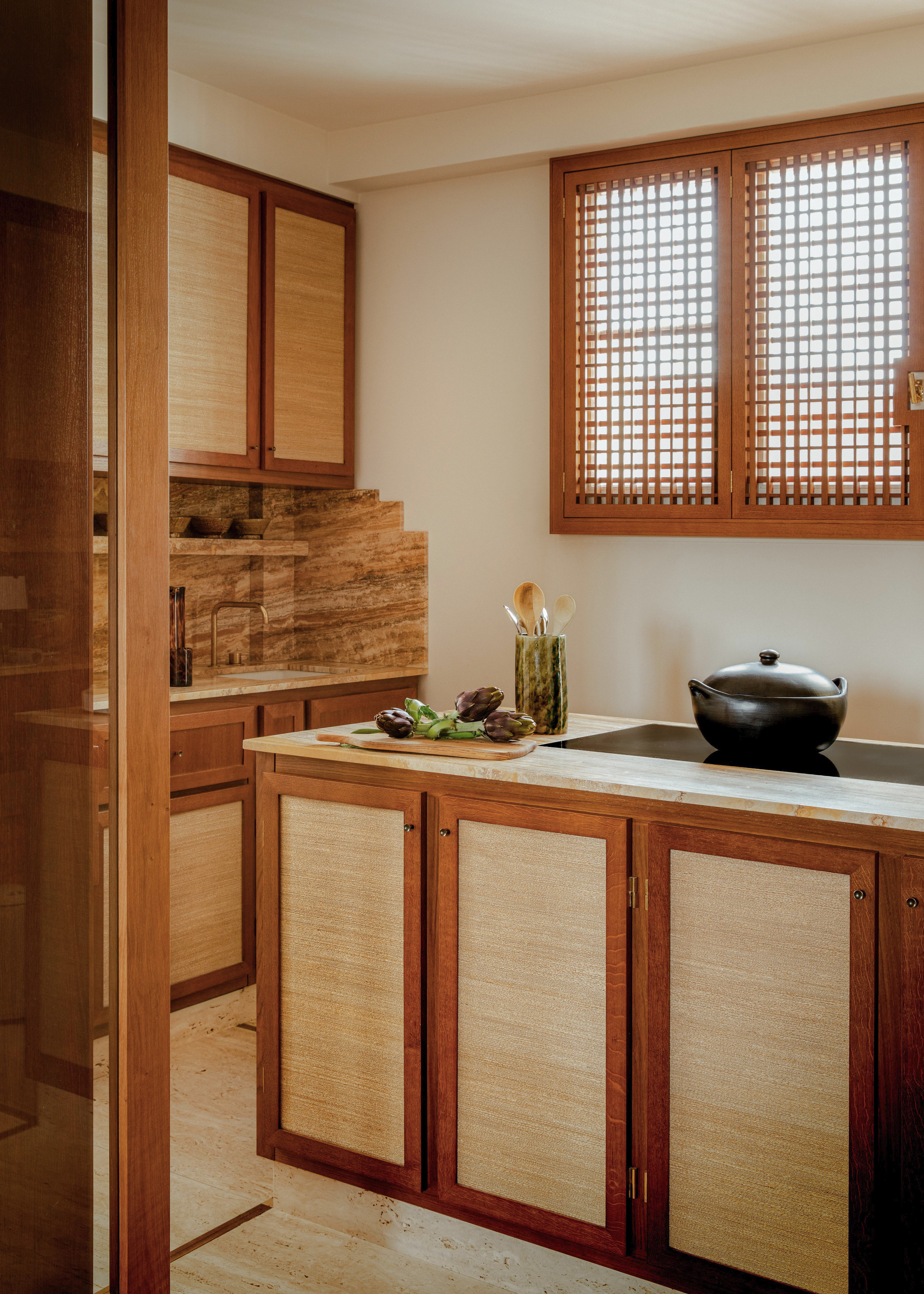 Rich wood kitchen with inset woven panels, beige and rust stone countertops and an island with inset hob