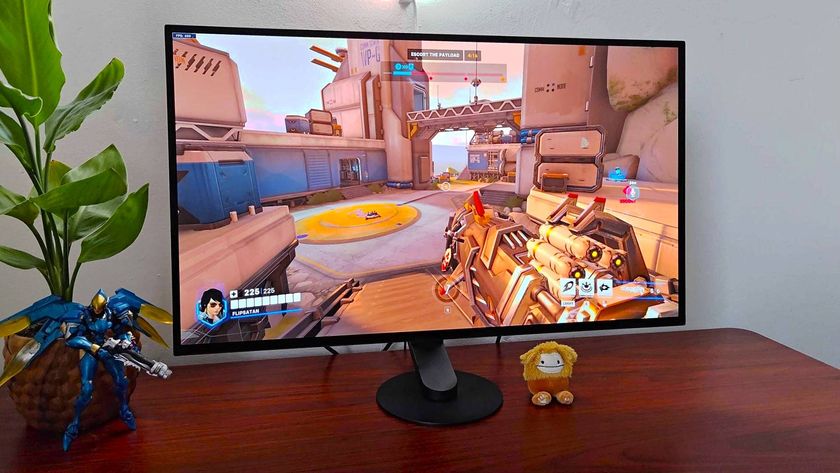 Sony Inzone M10S gaming monitor sitting on woodgrain desk next to plant and Pharah figure with Overwatch 2 gameplay in screen.