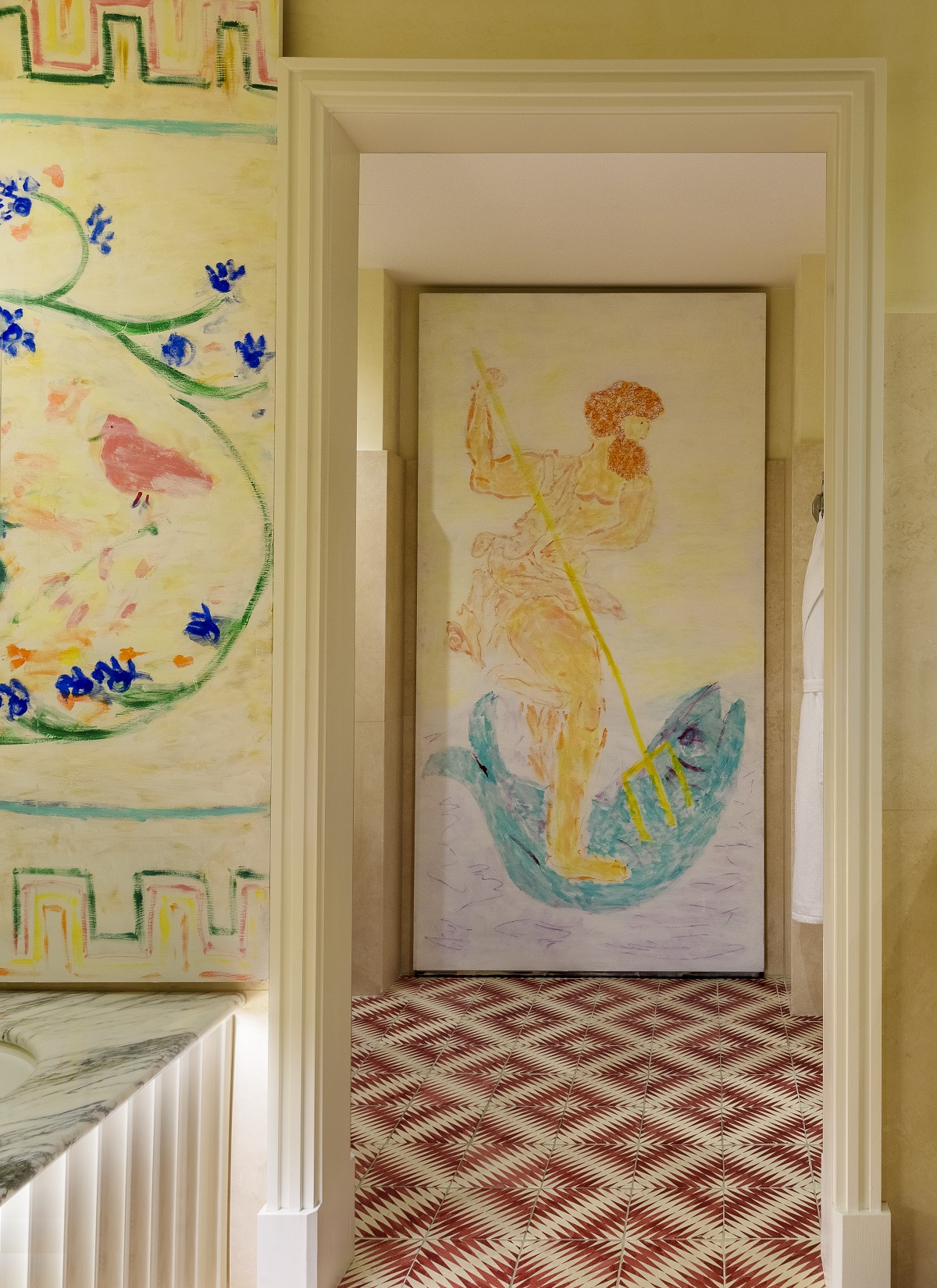 A hotel room with handrawn walls, marble countertops, tiled floors in bright red and white, and an ochre palette shows a Greek god fighting a fish with a trident, and other nature-inspired motifs.