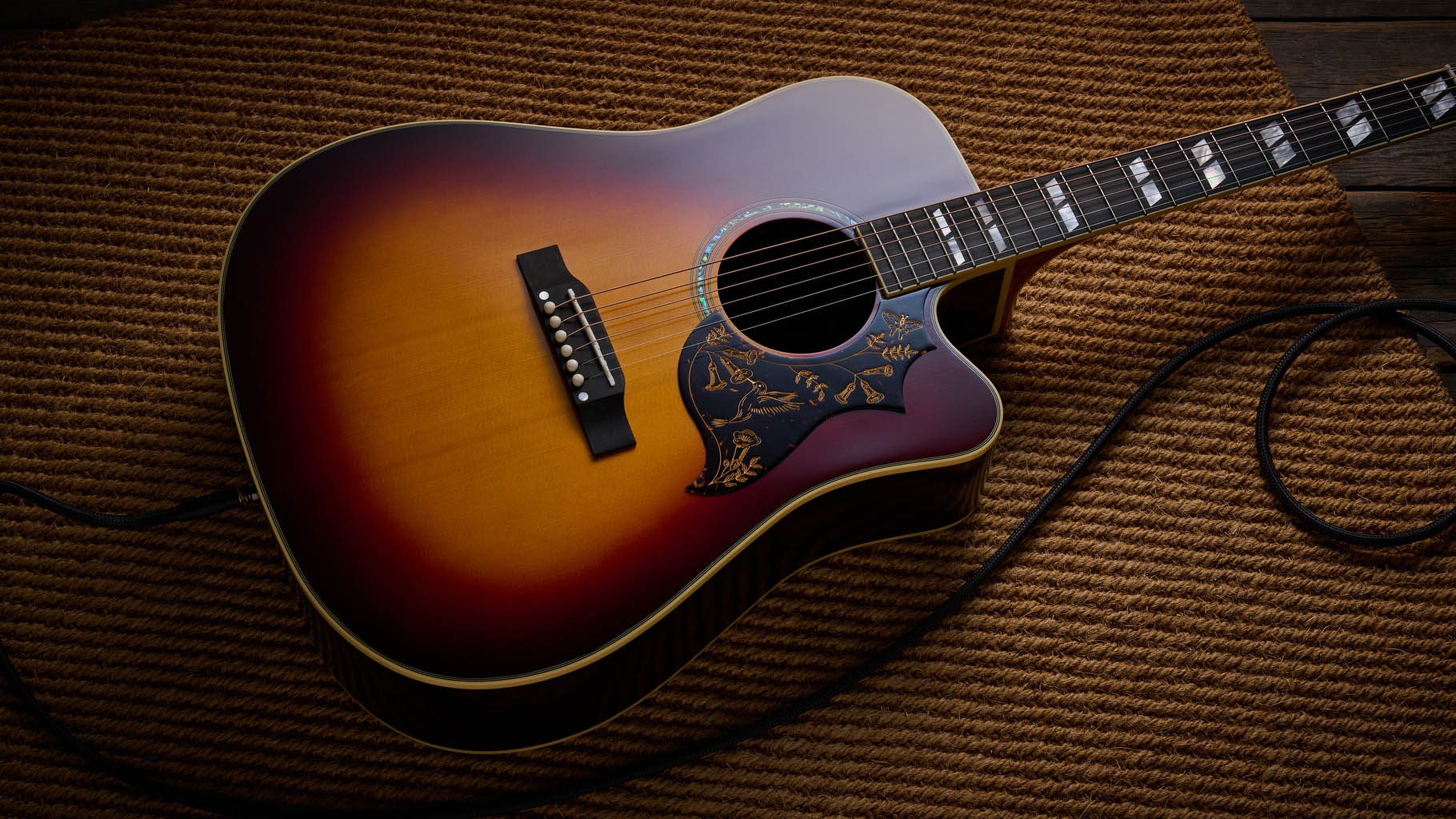 The Epiphone Inspired by Gibson Custom Hummingbird photographed in all its glory, in close-up and against a wheat-coloured rug.
