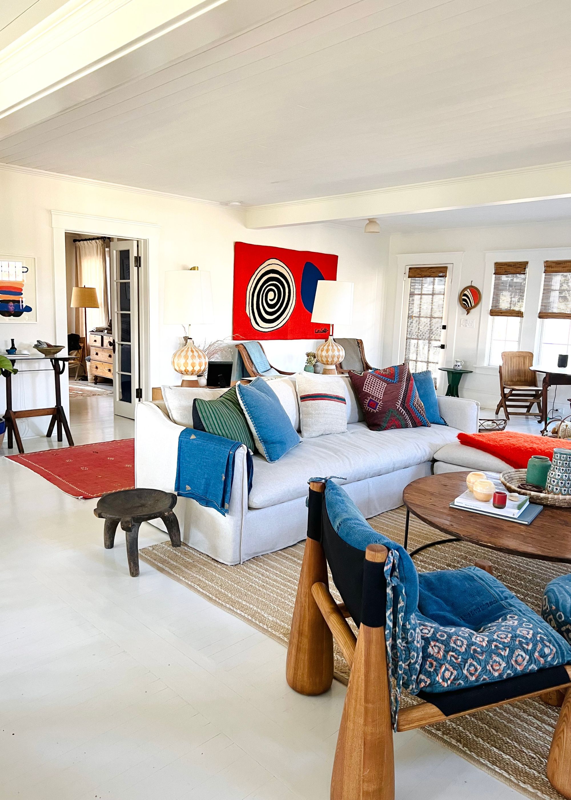 A blue chair with blue cushions scattered around. There is also a red run and red artwork placed in the home.