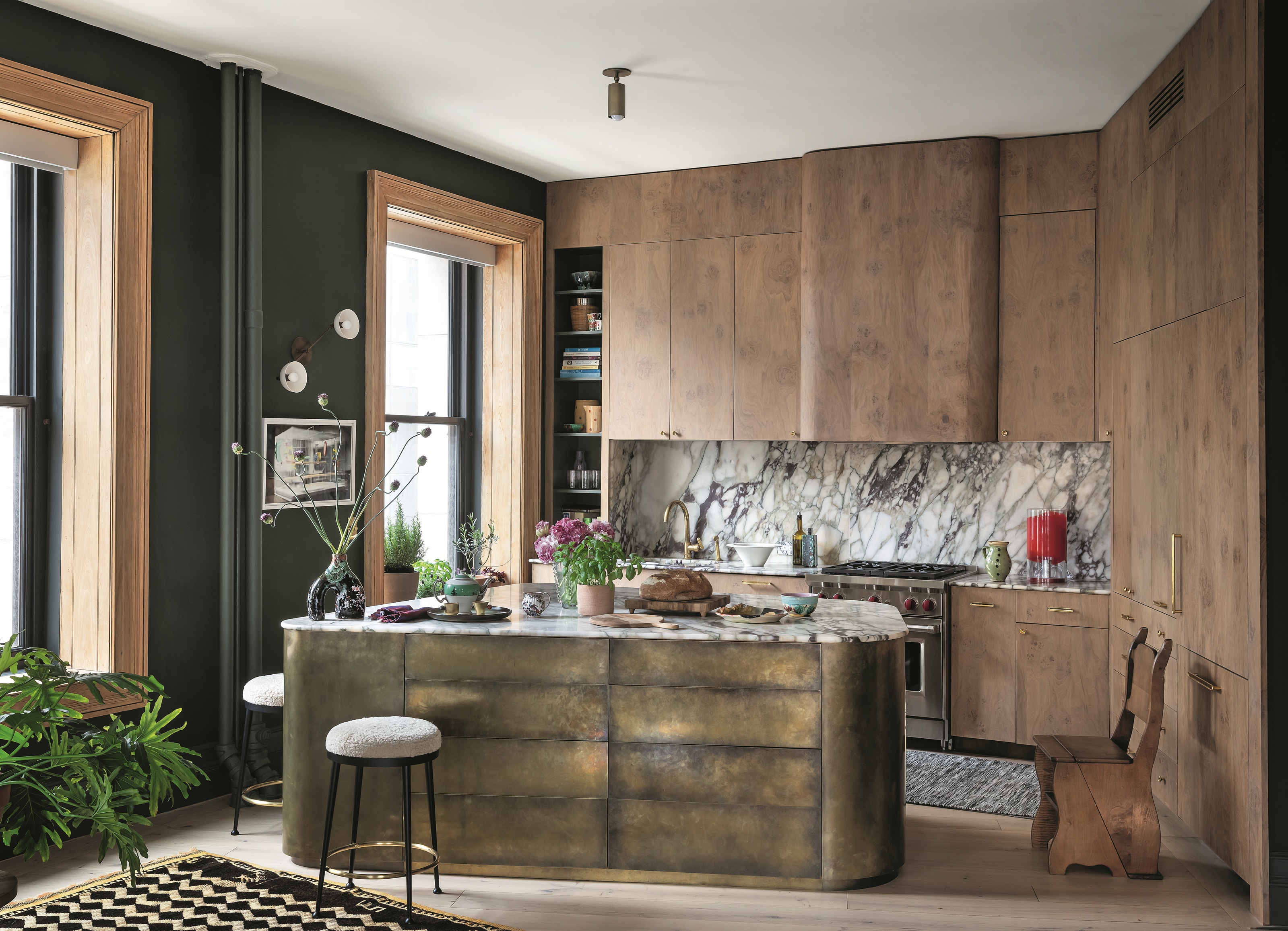 a kitchen with wood cabinetry, a marble splashback and an irregularly shaped brass island