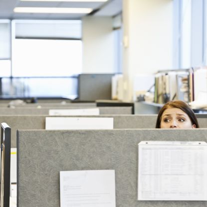 Woman peeping over desk partition in office