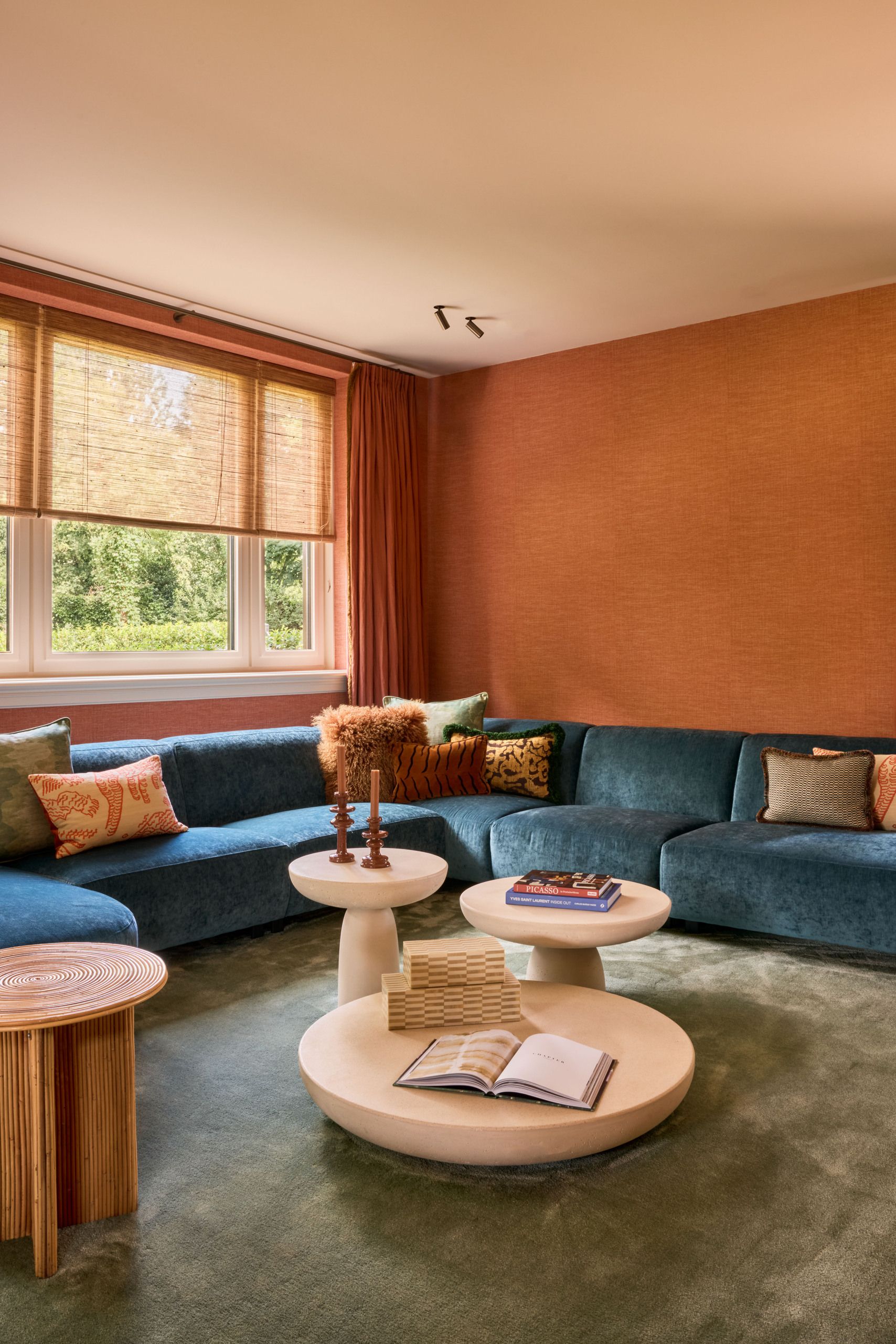 An orange living room with a sage green carpet, a teal blue corner sofa, and three nesting coffee tables.