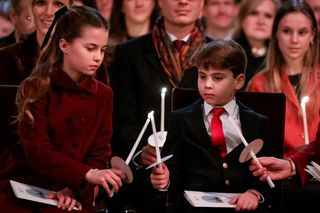 Princess Charlotte lighting a candle with Prince Louis sitting at a carol concert