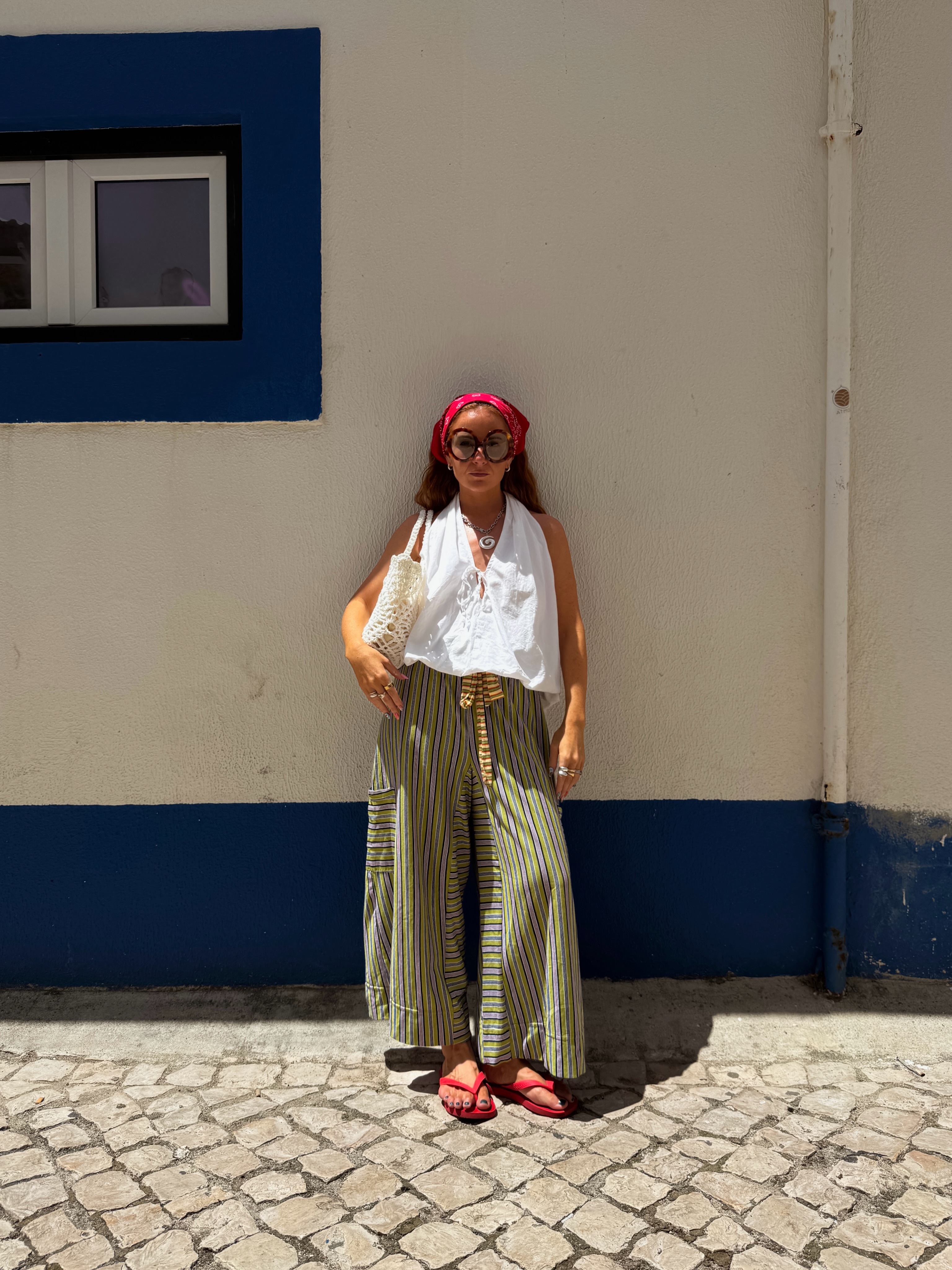 Influencer Rebecca Ferraz Wyatt wearing striped linen trousers with a white halterneck top and red flip flops.