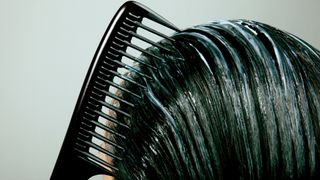 A close up of a woman combing a treatment/conditioner through her hair with a black comb