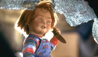 Child's Play Chucky holding a knife framed by a shattered car windshield