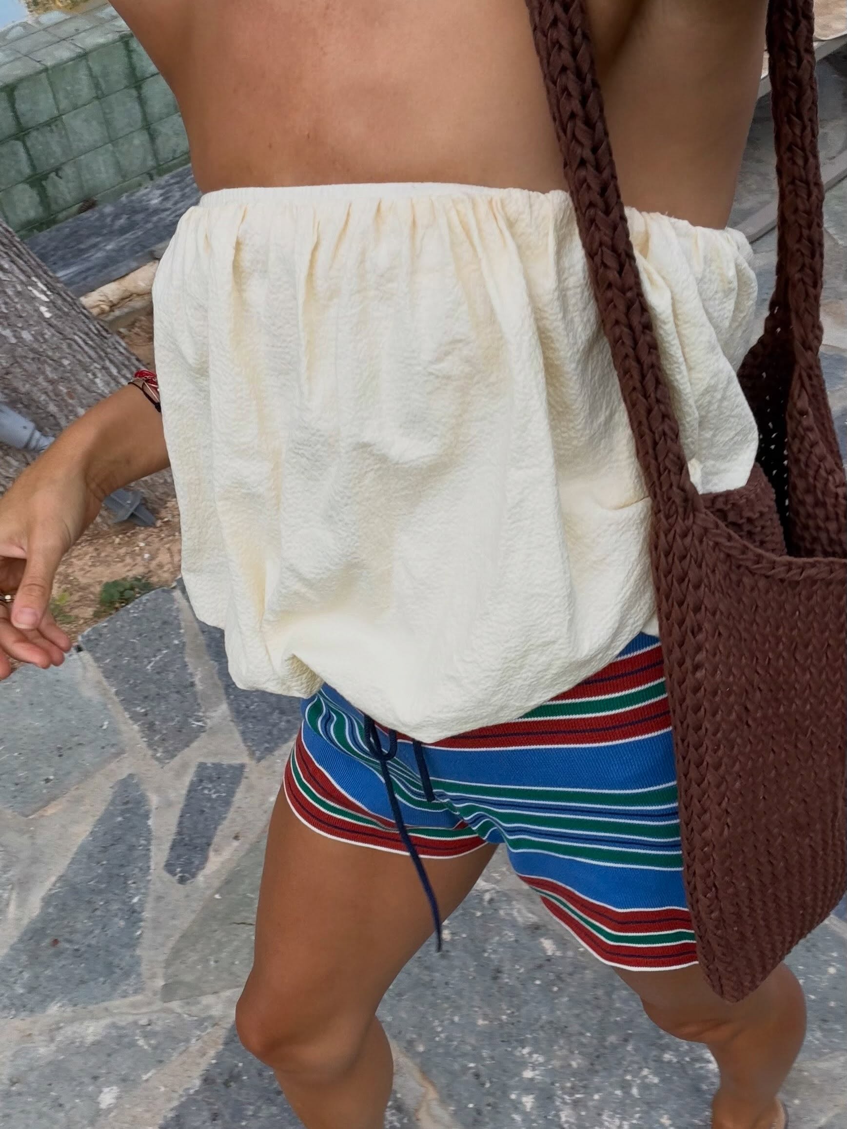 An image of an influencer wearing a white bandeau top, colourful striped shorts and a brown crochet bag
