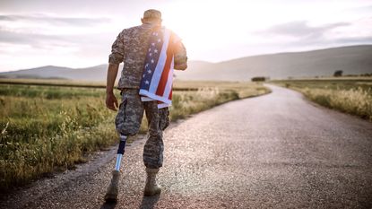 picture of an amputee soldier walking on a road with an American flag over his shoulder
