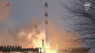 a white, red and green rocket launches into a blue sky.