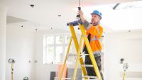 An electrician up some ladders working on overhead lights