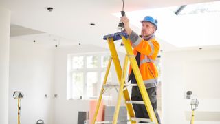 An electrician up some ladders working on overhead lights