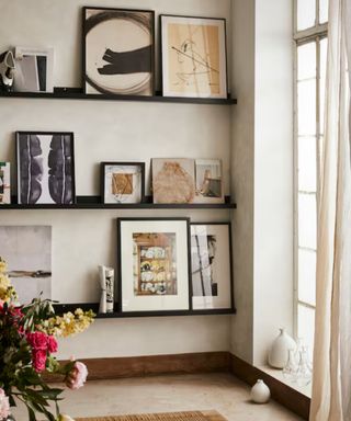 IKEA picture frames in a mix of sizes on black picture ledges in a neutral room with a large window and textured walls