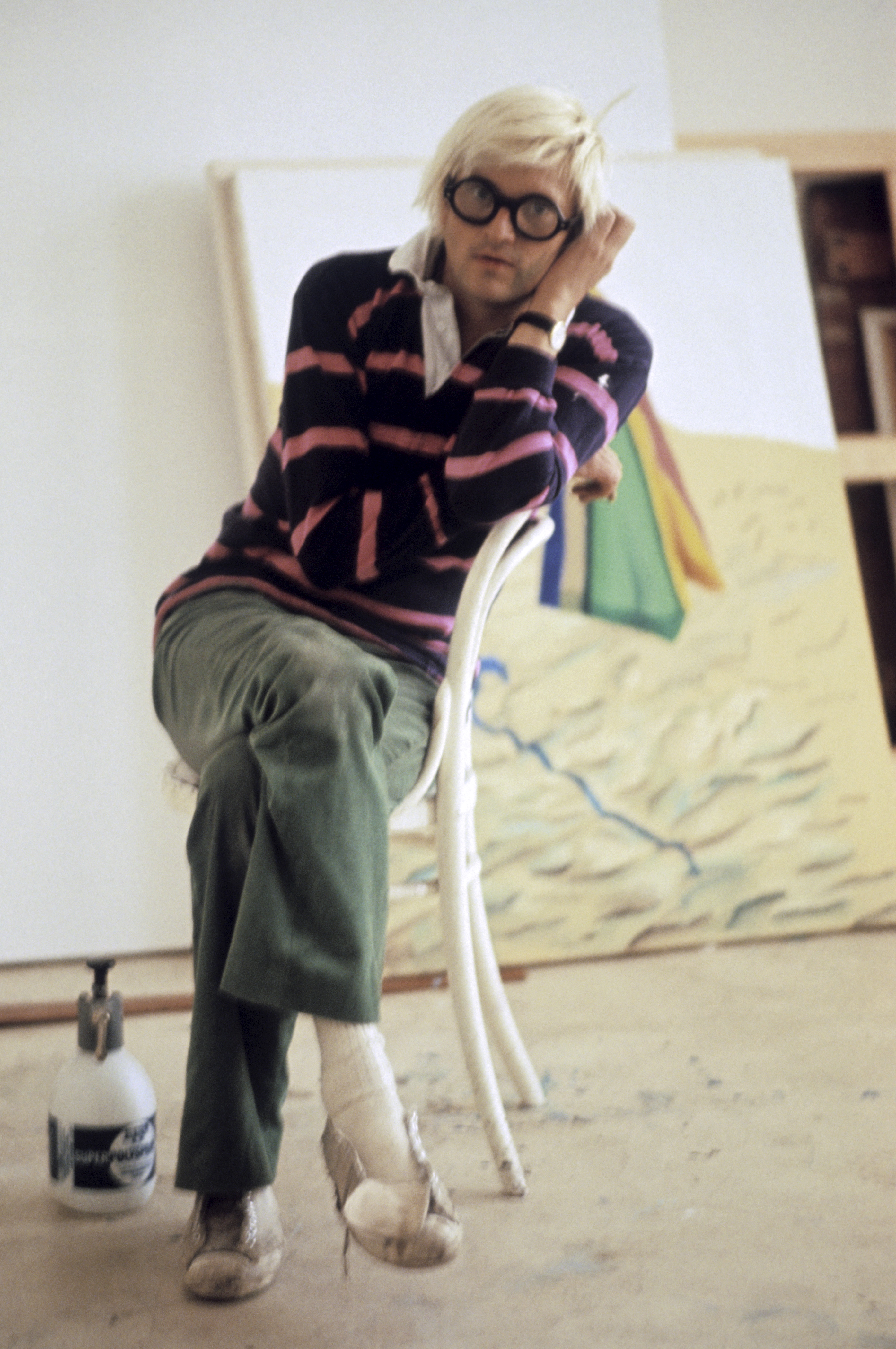 David Hockney photographed in 1971 in his studio while wearing a pink and blue rugby shirt