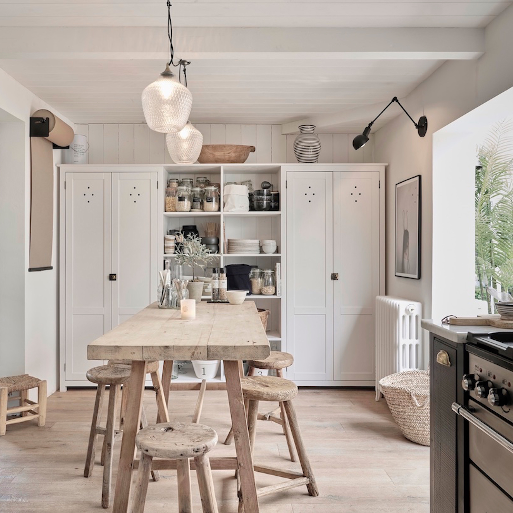 a kitchen diner with rustic wooden table and stools and a row of pantry cupboards at one end