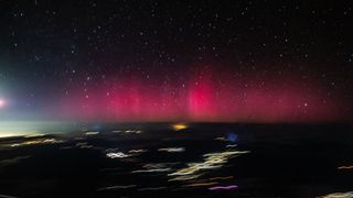 Fuzzy pink aurora lights stretch across the horizon as seen from an airplane