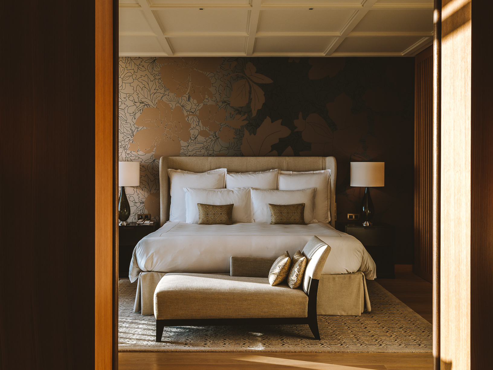 A minimalist hotel with cream tones throughout boasts floor-to-ceiling windows, historical accents, and a naturally lit atmosphere.