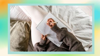 A woman sitting on her bed, using a note pad to write.