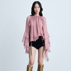 model wears pink blouse, black shorts, and tall boots